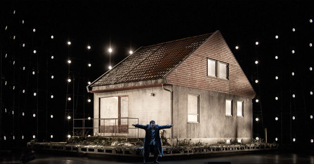 Kvinne med utstrakte armer foran hus