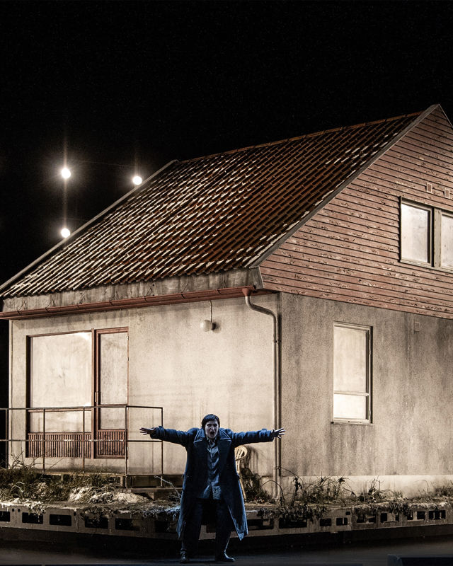 Kvinne med utstrakte armer foran hus