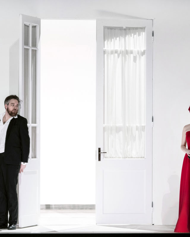 To menn i dress ser på en kvinne i lang, rød kjole