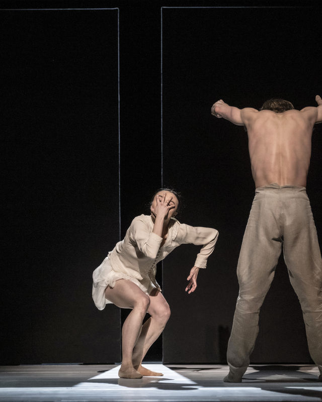 Kvinnelig danser holder hånden sin foran ansiktet, mann i bar overkropp står md ryggen til og hendene hevet