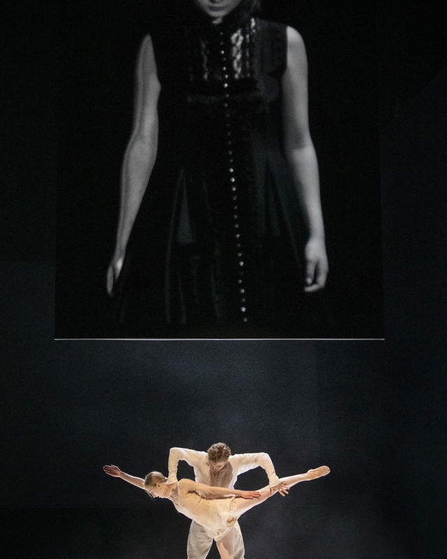 mann og kvinne som danser, stort bilde av ung jente er projisert på veggen bak dem