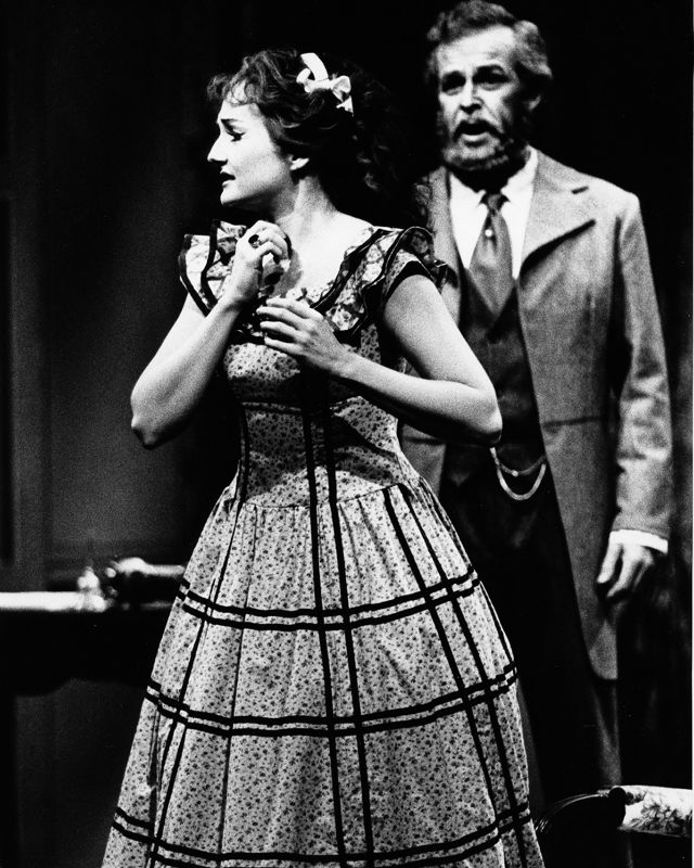 Gammelt svart-hvitt bilde fra operaforestilling, kvinne i kjole og mann i bakgrunnen