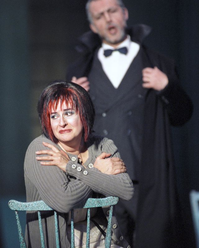 Gråtende kvinne på stol med mann i bakgrunnen