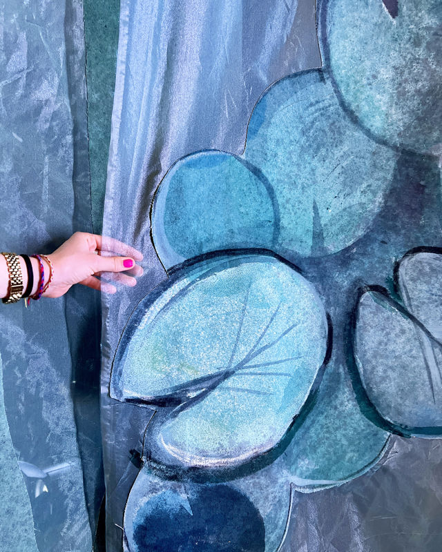 En hånd holder i et sceneteppe som viser blå-grønne vannliljer.