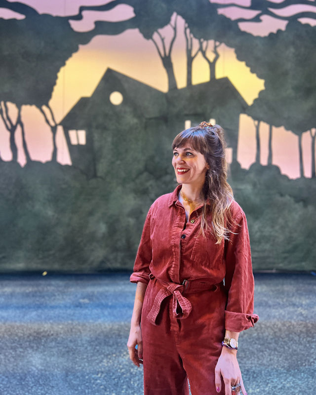 Portrett av scenografen foran sceneteppe av hus og skog