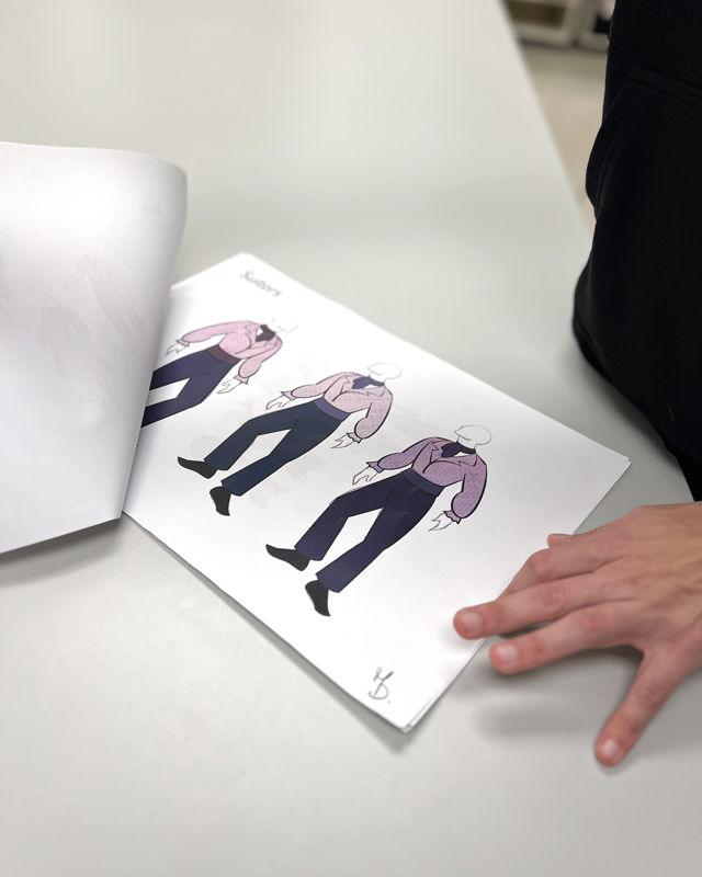 En hånd holder på et ark med kostymetegninger av herrekostyme i lilla