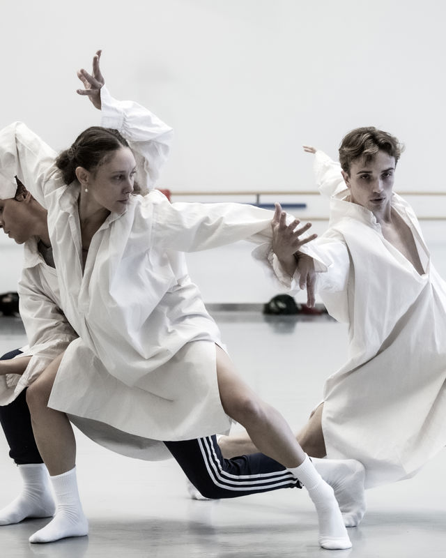 tre dansere i hvite kjortler og hvite sokker danser i studio