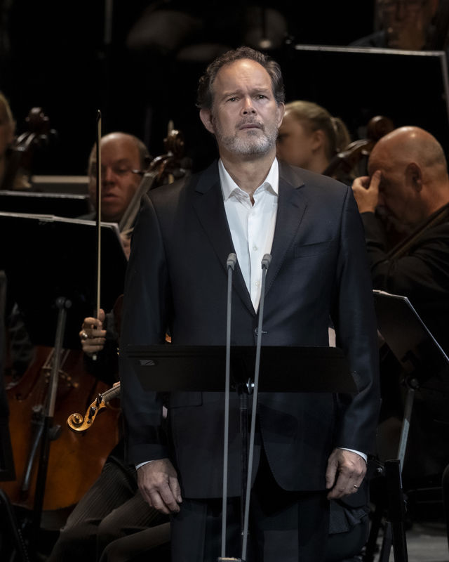 Mann i dress foran orkestermusikere