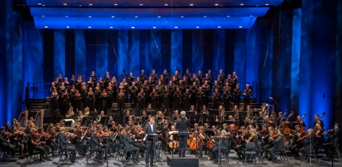 Mann i dress på scenen foran stort orkester og kor