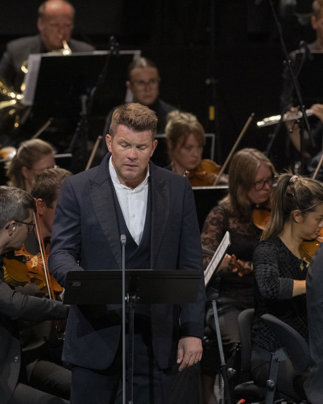Mann i dress foran orkestermusikere