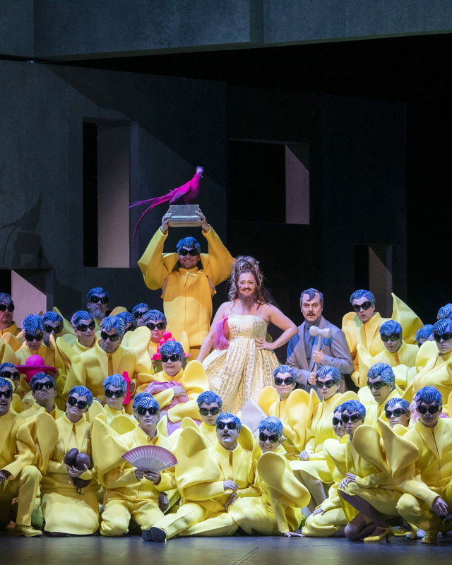 Mange mennesker i gule kostymer og blå parykker, kvinne med skjegg i midten