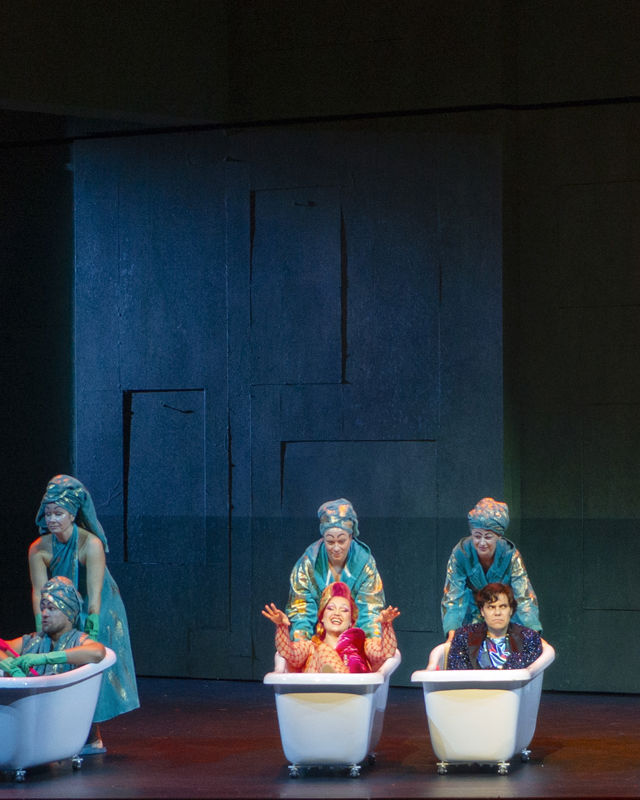 åtte mennesker sitter i badekar, blir skjøvet av andre med turkise kostymer