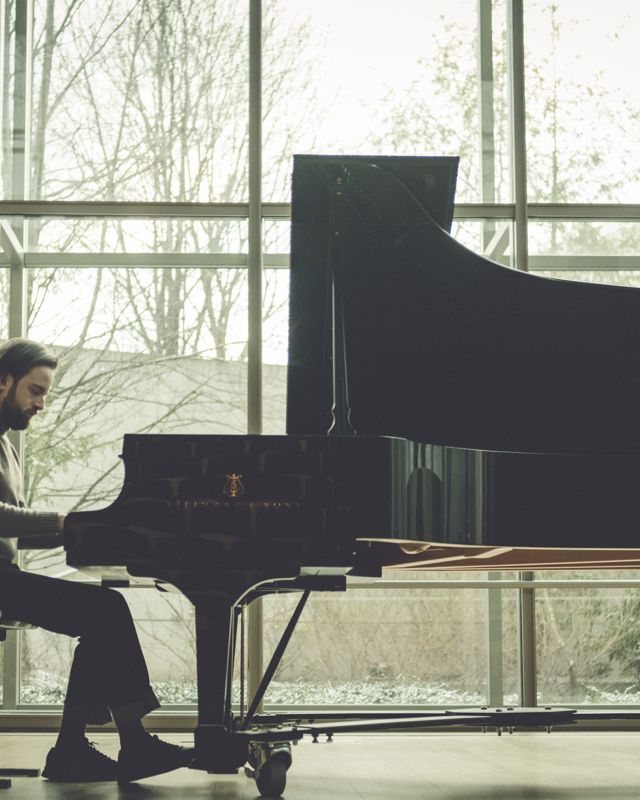 Mann spiller på flygel foran stort vindu